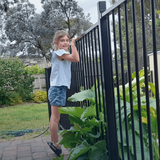 Child climbing a pool fence near plants, demonstrating a common non-compliance hazard under Victorian pool safety regulations