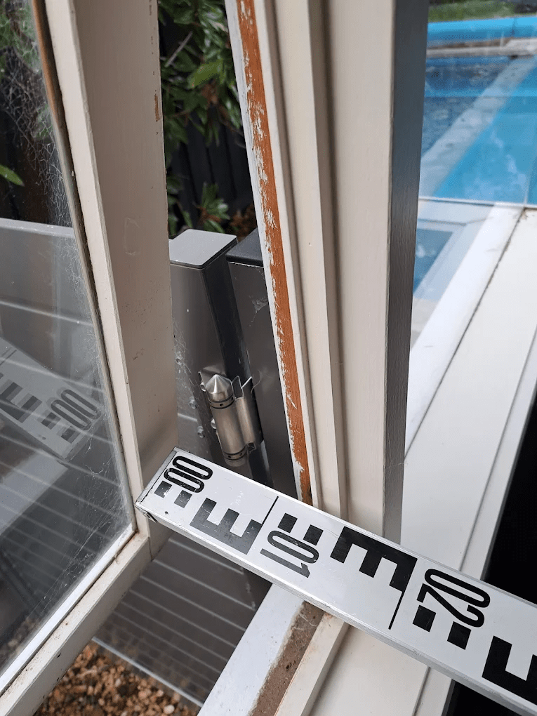 Measuring window gap near a pool fence to check Victorian 100 mm safety compliance rule in a Melbourne home.